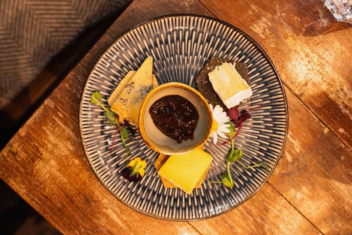 A plate of assorted cheeses with chutney, crackers, and decorative flowers served on a rustic wooden table..jpg