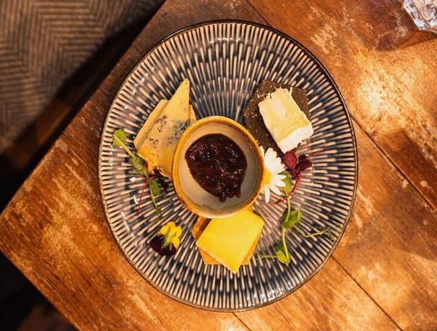 A plate of assorted cheeses with chutney, crackers, and decorative flowers served on a rustic wooden table..jpg