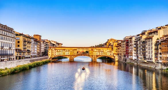 photo of golden sunset over ponte vecchio bridge with traditional boat on the arno river, Florence, Italy.