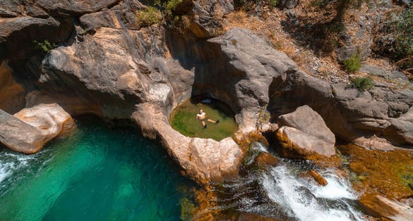 photo of a male traveler bathes in a cold mountain river. To swim at Sapadere canyon and waterfall in Summer sunny day. Antalya, Turkey.
