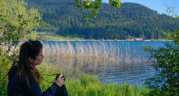 photo of young woman photographer sitting and taking photo on the edge of an attractive lake. Abant Gol (Paradise Lake), Bolu ,Turkey.