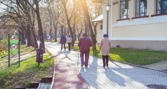 Elderly women and young couple walk along the park path. One of the women using nordic walking poles. Nyiregyhaza, Hungary