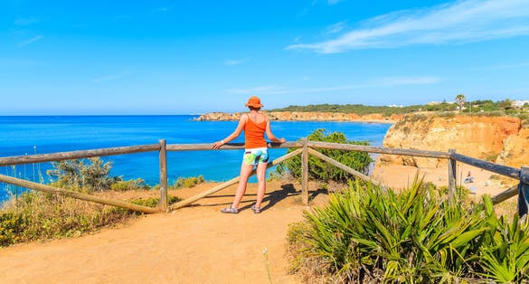 Photo of tourist standing on cliff and looking at beautiful sea coast, Portimao town, Portugal