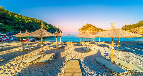 Photo of beach, chairs and umbrellas at sunrise in Paleokastritsa village, Corfu island, Greece.
