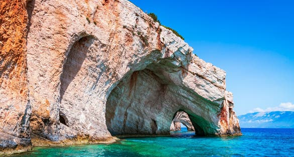 Photo of rock arches of blue Caves from sightseeing boat in blue water of Ionian Sea near Agios Nikolaos.