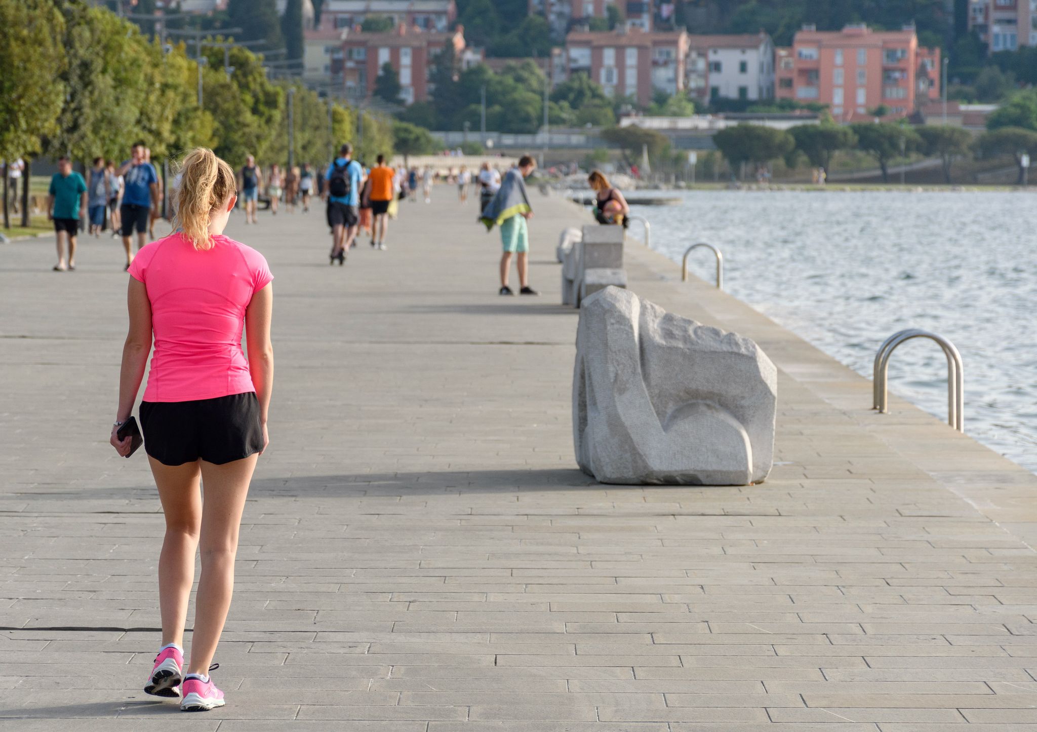 The Woman wearing pink sports top and shorts, walking on the waterfront promenade in Koper, Slovenia