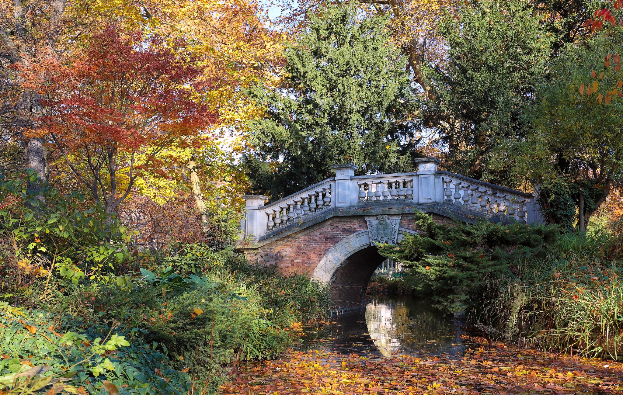 photo of the autumn trees and small bridge in Parc Monceau, Paris, France. The park is unusual in France due to its English style, with informal layout, curved walkways and randomly placed statues.