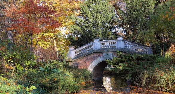 photo of the autumn trees and small bridge in Parc Monceau, Paris, France. The park is unusual in France due to its English style, with informal layout, curved walkways and randomly placed statues.