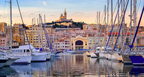 Yachts reflecting in the still water of the old Vieux Port of Marseilles beneath Cathedral of Notre Dame, France, on sunrise