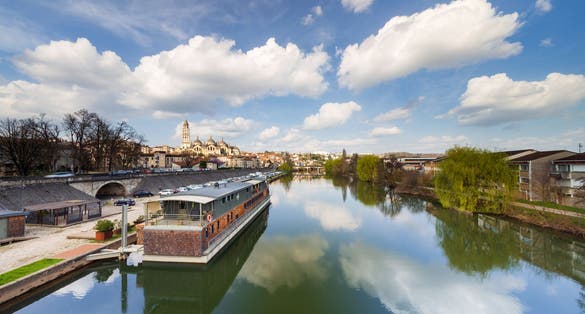 Wide sunset view of the Isle river with a barge or houseboat and the Saint Front cathedral in the background from the bridge Saint George. Perigueux.