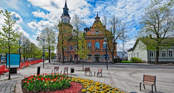 Ornate flowerbed with wooden chairs around in front of old historic buildings in the center of Rauma, Finland
