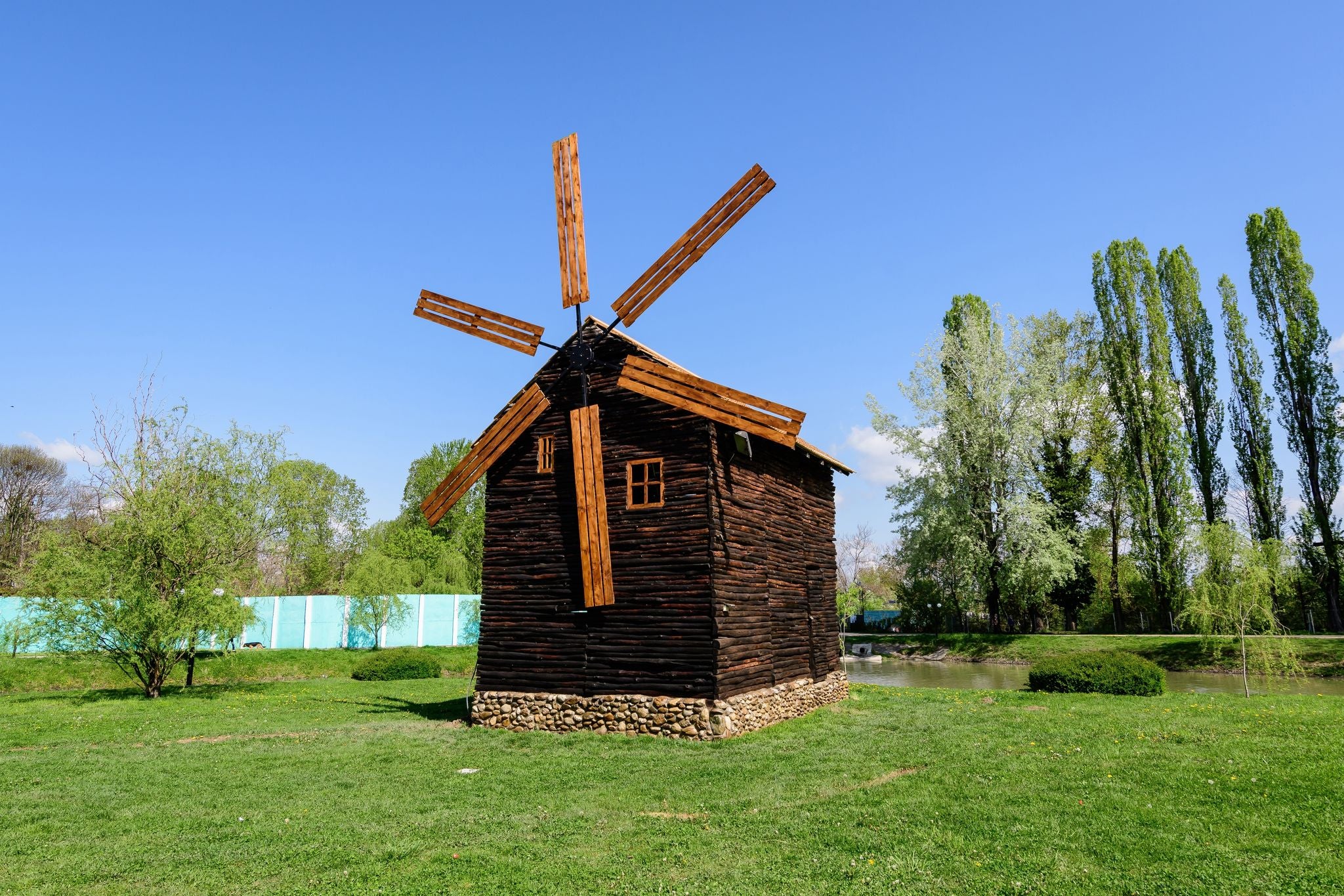 Decorative old wood mill and green grass on a small island on the lake from the Chindiei Park (Parcul Chindiei) in Targoviste, Romania, in a sunny spring day
