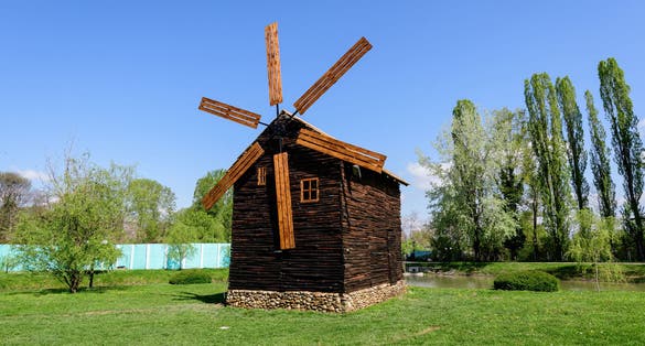 Decorative old wood mill and green grass on a small island on the lake from the Chindiei Park (Parcul Chindiei) in Targoviste, Romania, in a sunny spring day