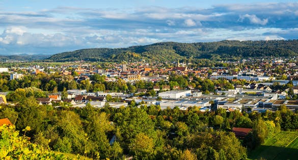 Germany, Wide aerial view above houses, church and roofs of schorndorf city in valley between forested hills in warm evening sunset light