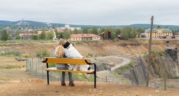 photo of a girl and dog on the bench next to Falun copper mines in Sweden. Huge colorful hole in the ground. Place where typical Swedish red color got name. Falun town in the background. Scandinavia.