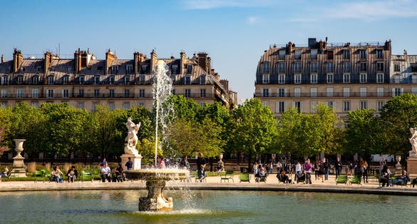 Photo of Water splashing in a fountain in the Tuileries Gardens,Jardin des Tuileries in French, with people relaxing in the sun in the background, France.