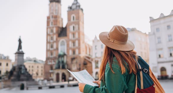 Photo of female tourist is exploring new city ,holding a paper map on Market Square in Krakow, Poland.