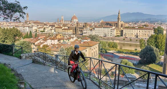 cheerful senior woman cycling with her electric mountain bike above downtown of Florence with stunning view over the old city, Tuscany, Italy