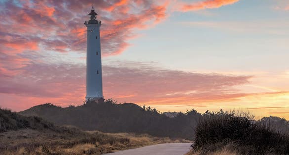 Photo of the 38 meter tall Lyngvig Lighthouse at beauttiful sunset built in 1906, on the Danish North Sea coast serves as a beautiful tourist attraction amongst the sand dunes.