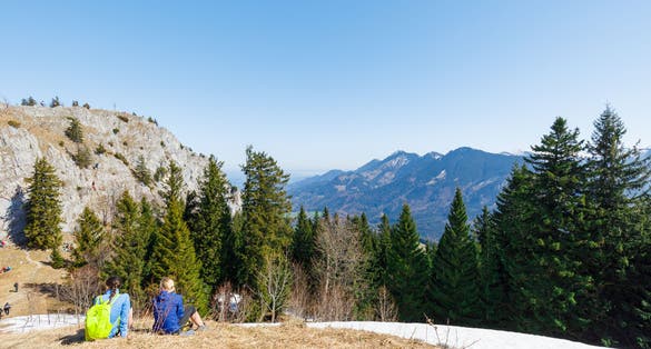 two young women sitting summit of partly snow covered Mountain Heuberg, Nussdorf, Rosenheim, enjoying spring time, Bavaria