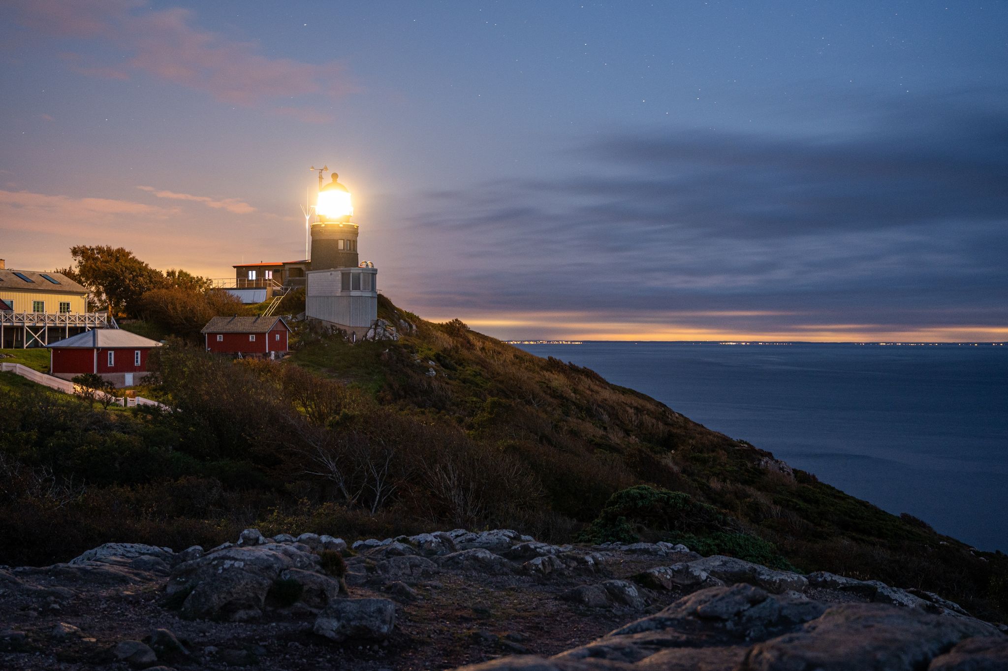 photo of Kullen lighthouse shining its light after sunset. Denmark and Sweden in the background.