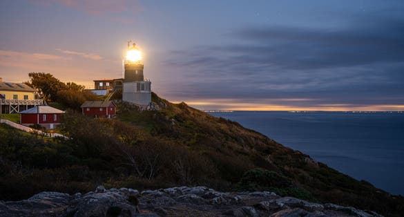 photo of Kullen lighthouse shining its light after sunset. Denmark and Sweden in the background.