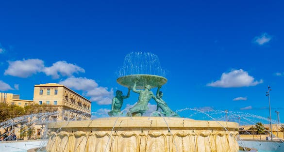 Photo of the famous Triton fountain, three bronze Tritons holding up a huge basin, in front of the City Gate in Valletta.