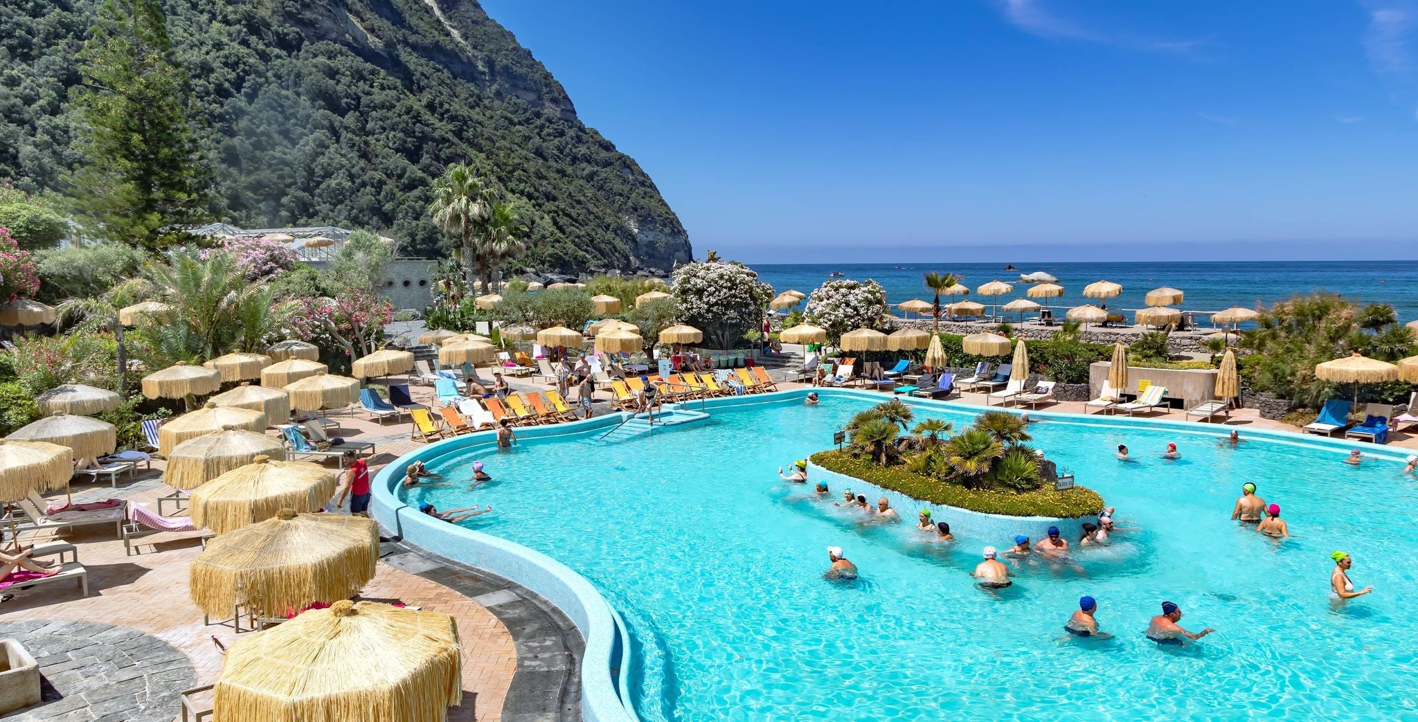 People swimming in a thermal pool at a seaside resort in Italy in June with sun loungers and umbrellas..jpg