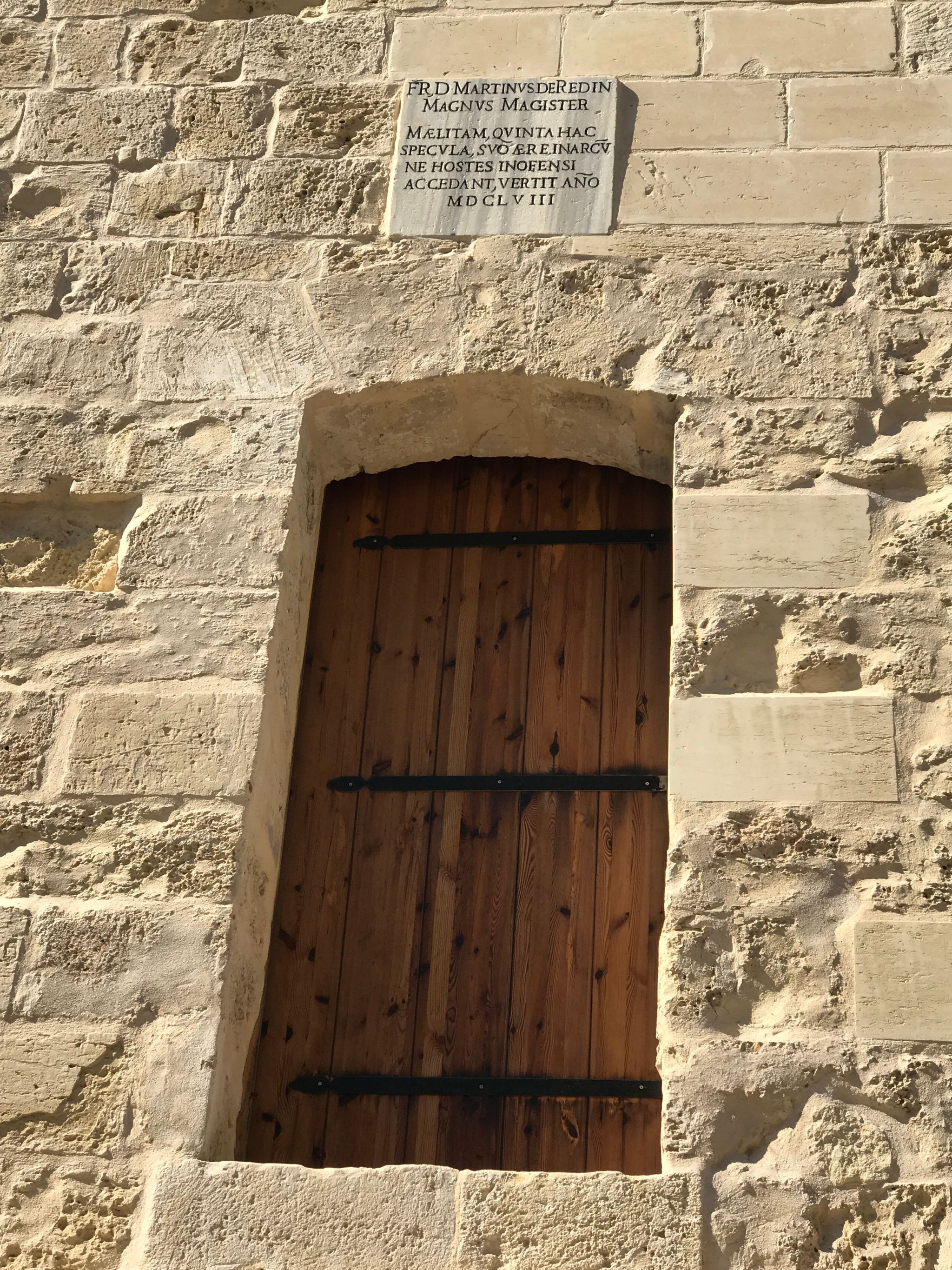 A wooden door set back into buttery sandstone, part of s tower defence in Malta.