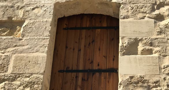 A wooden door set back into buttery sandstone, part of s tower defence in Malta.