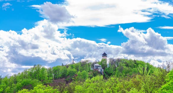 Photo of Diana Observation Tower (Rozhledna Diana) and funicular on hill above Slavkov Forest with green trees and Karlovy Vary (Carlsbad) town, Czech Republic.