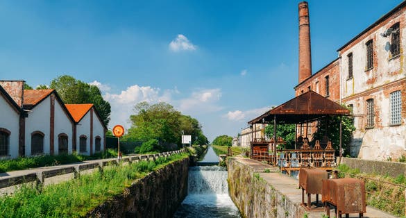 Old industrial warehouses alongside a cascade on a lock at the Naviglio Pavese, a canal that connects the city of Milan with Pavia, Italy