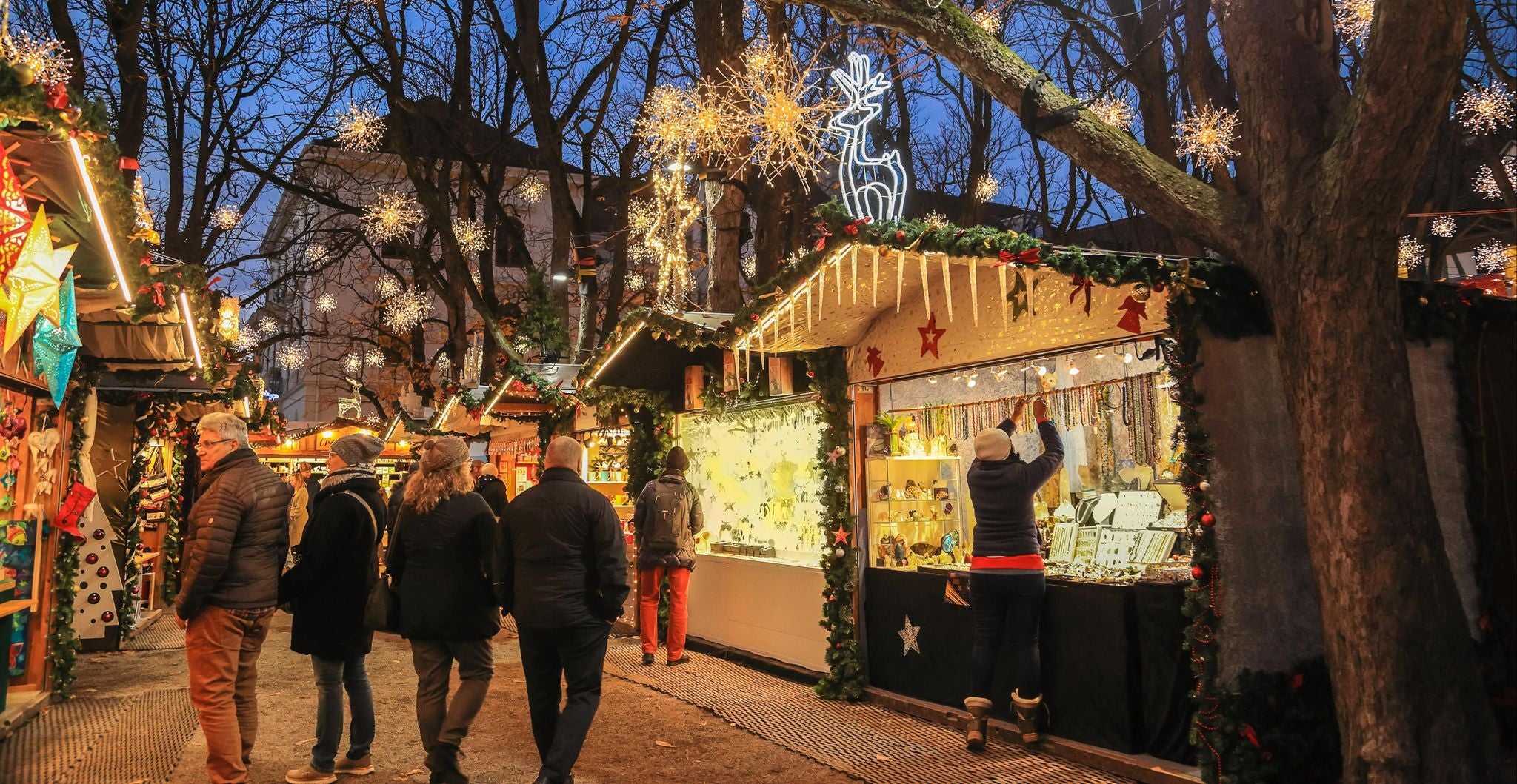 Shoppers browsing decorated stalls at Basel Christmas Market under glowing lights and trees..jpg