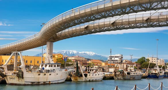 Photo of Ponte del Mare (Sea Bridge) and boats anchored in the harbor in the channel of the Pescara River and the Majella mountain in the background