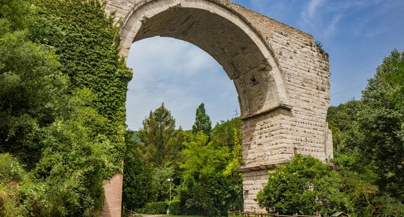 The ruins of the Roman arch bridge of Augustus, in Narni, Terni, Umbria. The remains of the bridge over the Nera river. The big and ancient stone arch, against the blue sky. Trees and dense vegetation