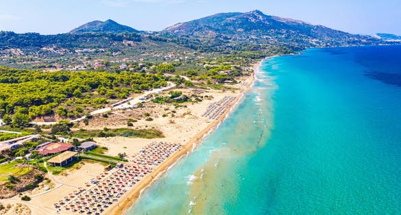 Photo of top view aerial drone view of Banana beach with beautiful turquoise water, sea waves and red umbrellas, Zakynthos Island, Greece.