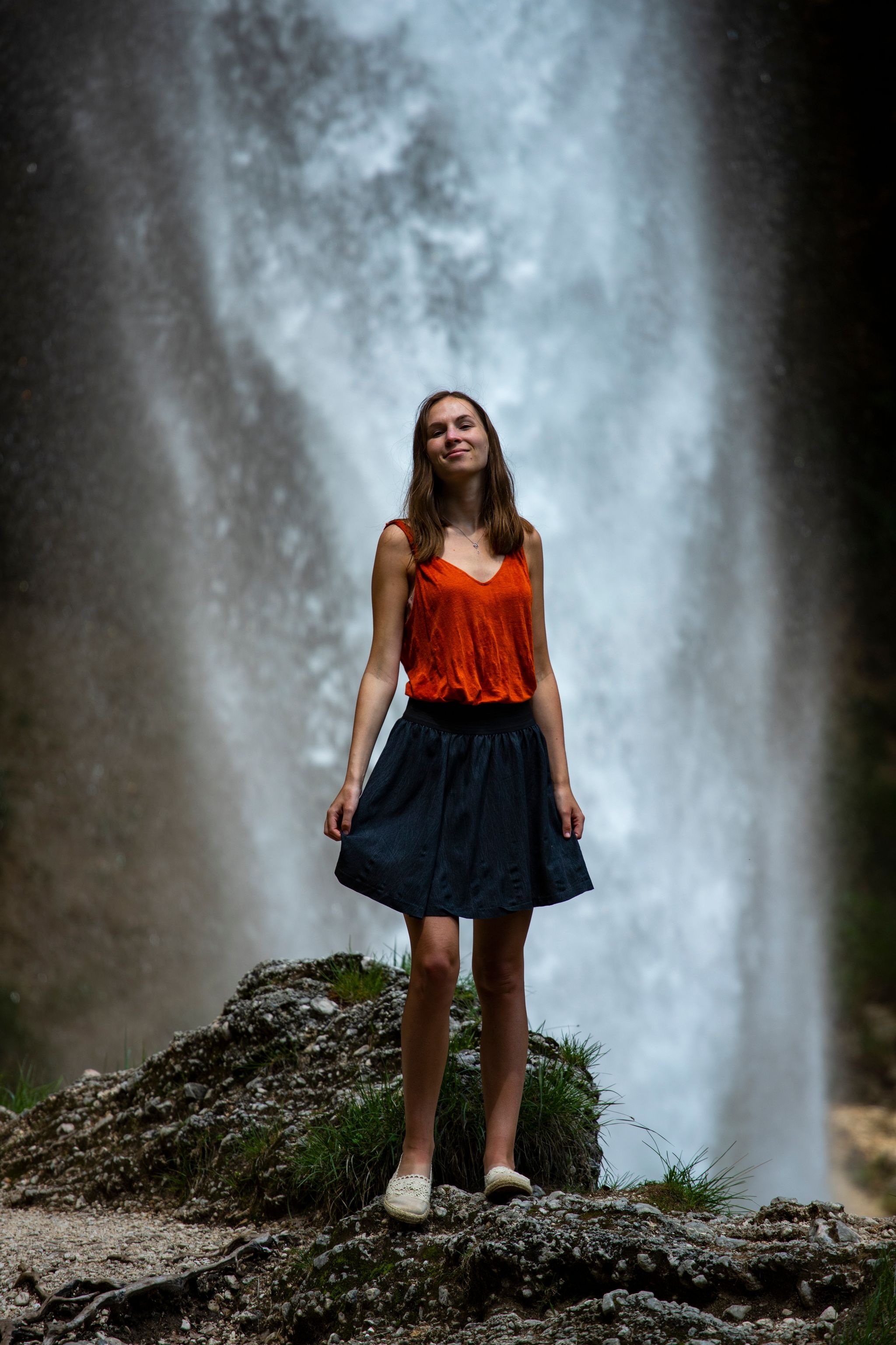 beautiful girl in a skirt stands in front of a powerful waterfall in slovenia, Peričnik falls