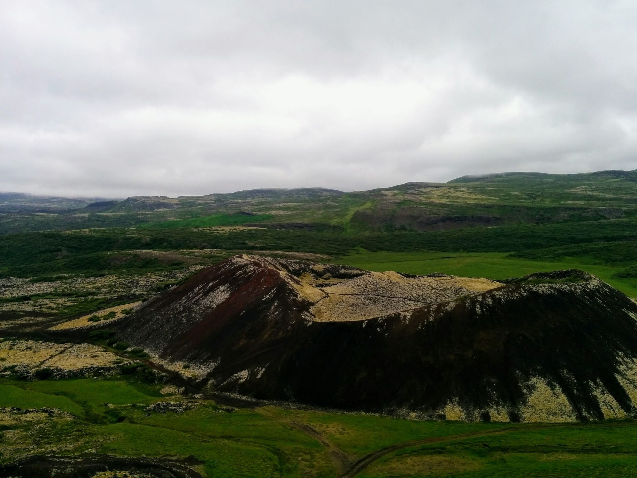 photo of a small crater of a dormant volcano Grabrok in the middle of a scenic hilly terrain; tundra landscape in polar summer; Iceland .