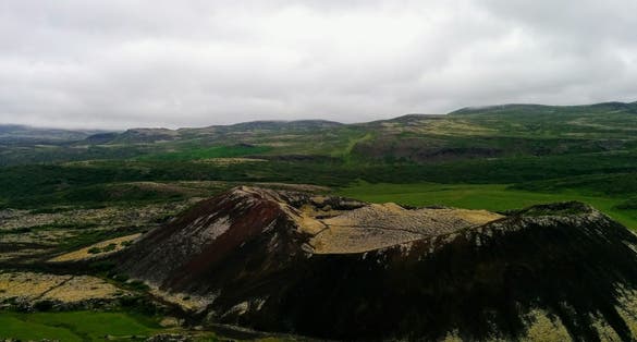 photo of a small crater of a dormant volcano Grabrok in the middle of a scenic hilly terrain; tundra landscape in polar summer; Iceland .