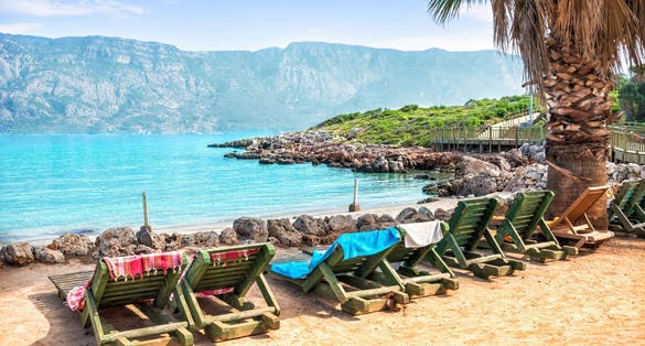 Photo of stones on the shore and wooden deck chairs on Cleopatra Island, Aegean Sea, Marmaris, Turkey.
