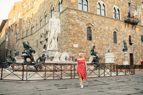 photo of front view of beautiful blonde female in red standing on piazza della signoria at old town. Woman walking and discovering streets of old Italy town. 
