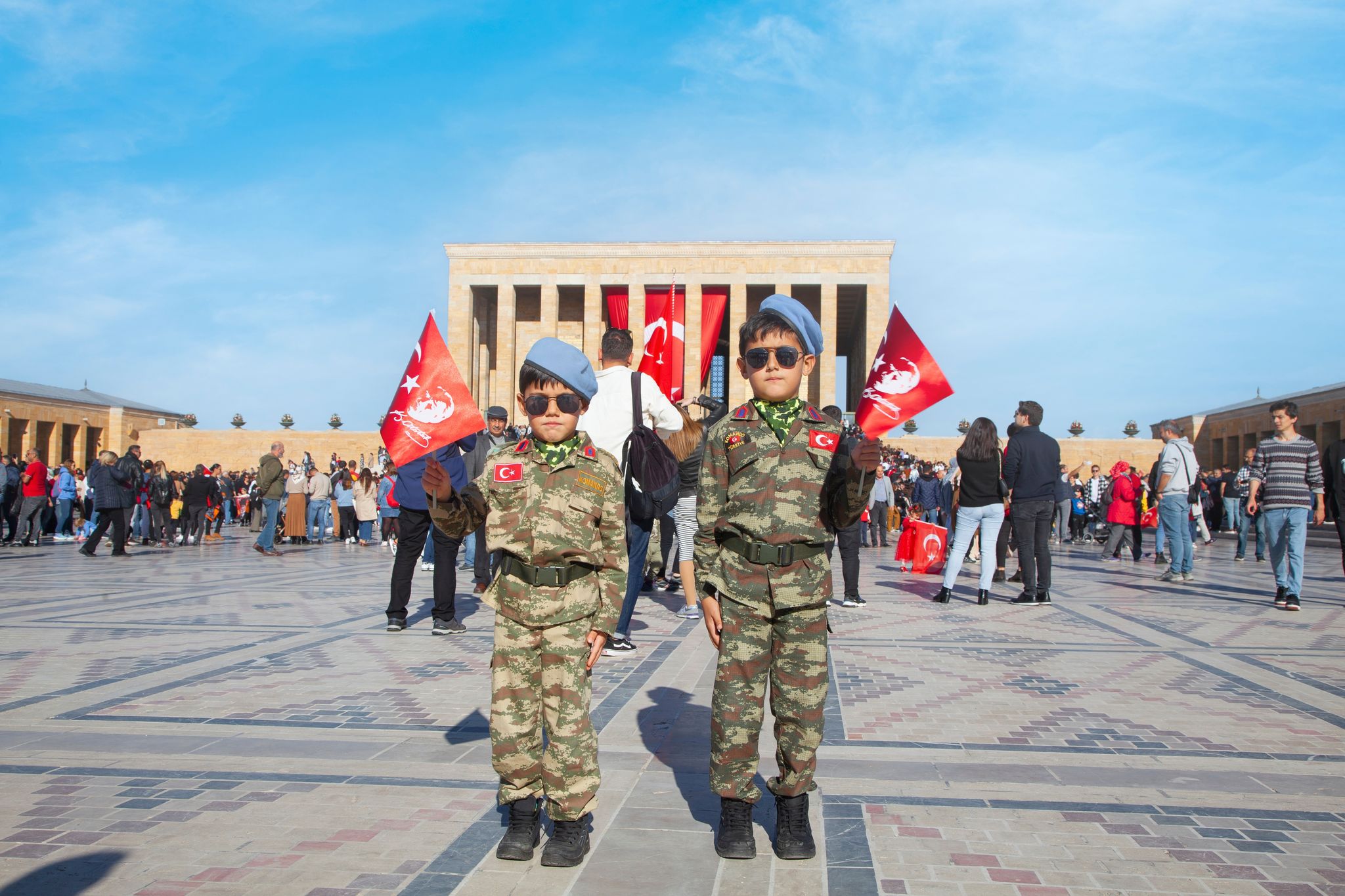  Two serious boys in military uniforms, sunglasses, blue berets and holding Turkish flag. 