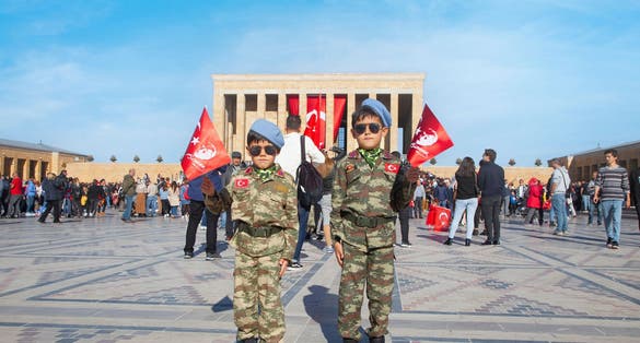  Two serious boys in military uniforms, sunglasses, blue berets and holding Turkish flag. 