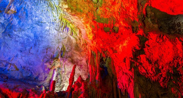 Photo of Prometheus Cave Natural Monument, Kutaisi, Georgia, with hanging stone curtains, stalactites and stalagmites, colorful illuminated rock formations.