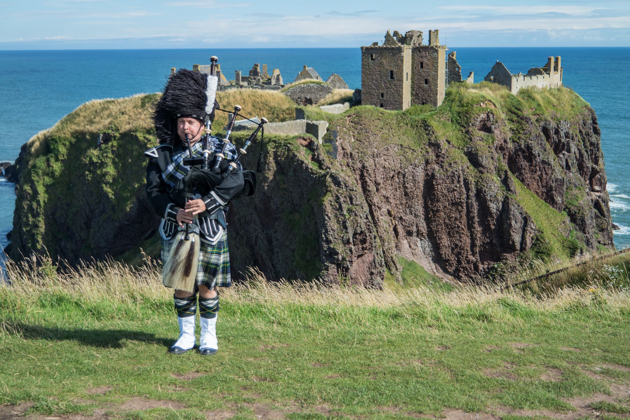 Traditional scottish bagpiper in full dress code at Dunnottar Castle in Stonehaven.