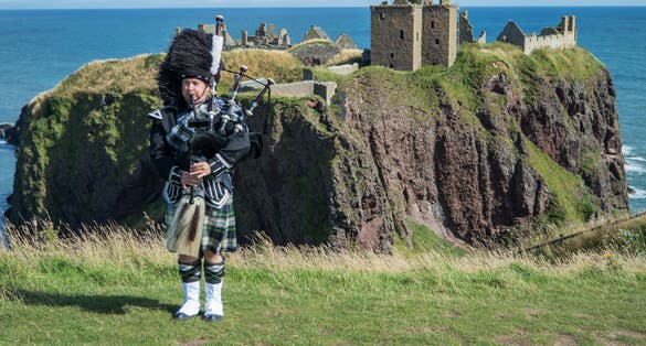 Traditional scottish bagpiper in full dress code at Dunnottar Castle in Stonehaven.