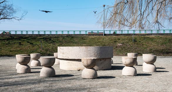 Photo of Stone table and stones - Table of Silence. Crows flying in the blue sky. A walk on a spring day through the park in Targu Jiu.