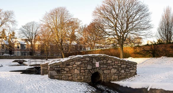 Photo of A small water stream coming under a scenic stone bridge in Westburn park, Aberdeen, Scotland .