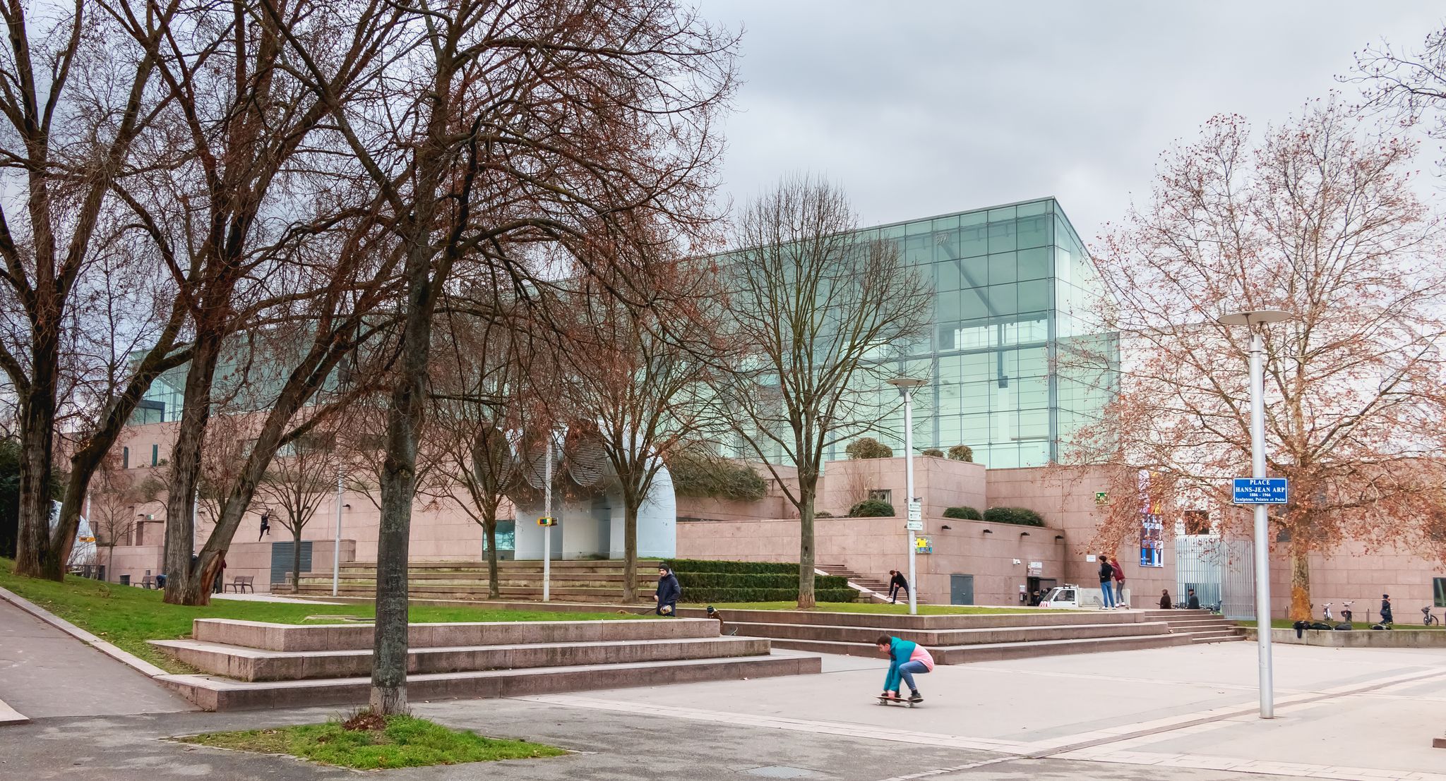 Architectural detail of the Museum of Modern and Contemporary Art in Strasbourg on a winter day in front of which young people are skateboarding.