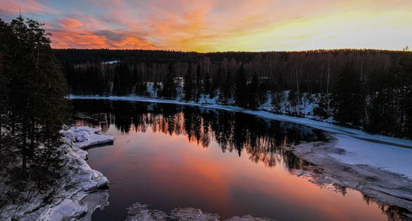 photo of view of A landscape of a pond surrounded by a forest during a breathtaking sunset in Hamar, Norway.
